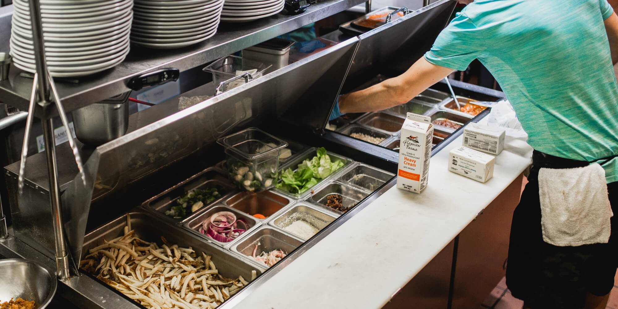 A person is grabbing prepped food from a Steelheart Prep table.