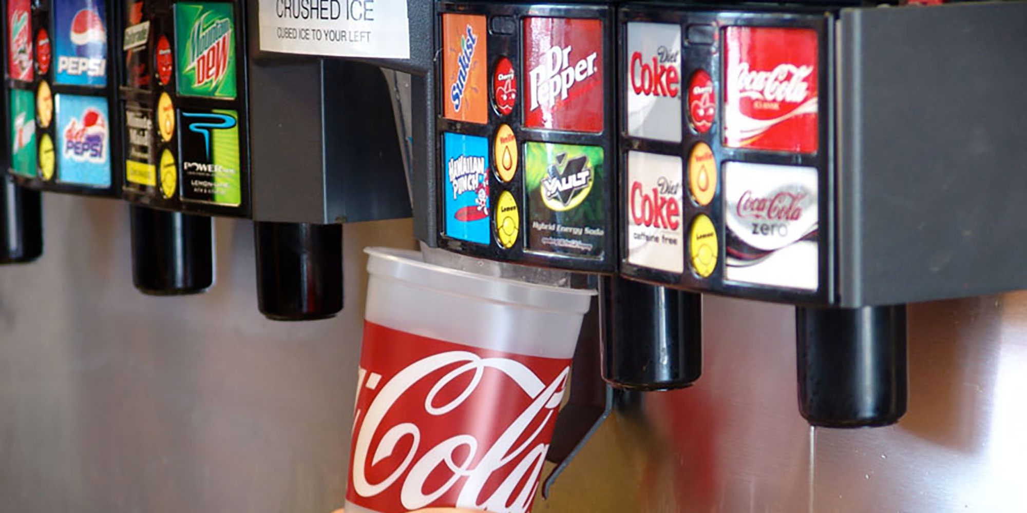 A person is pushing a soda cup under the ice dispenser on a soda machine.