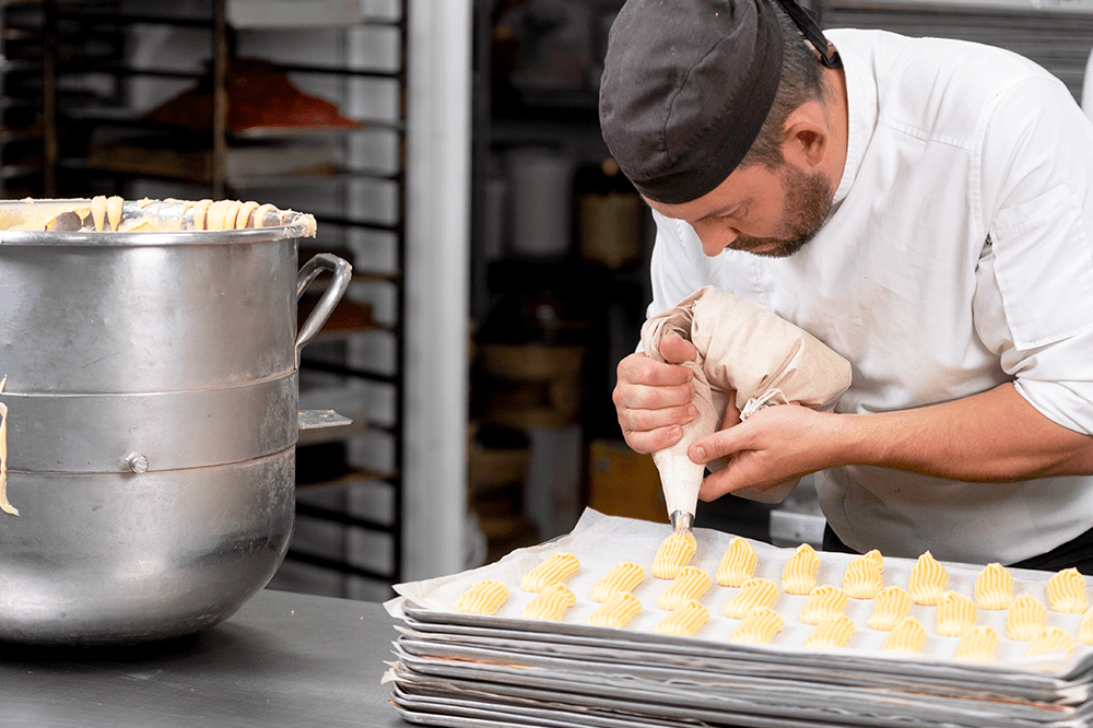 Pastry chef piping dough in commercial kitchen with Hoshizaki dual temp unit nearby for flexible refrigerated and frozen storage.