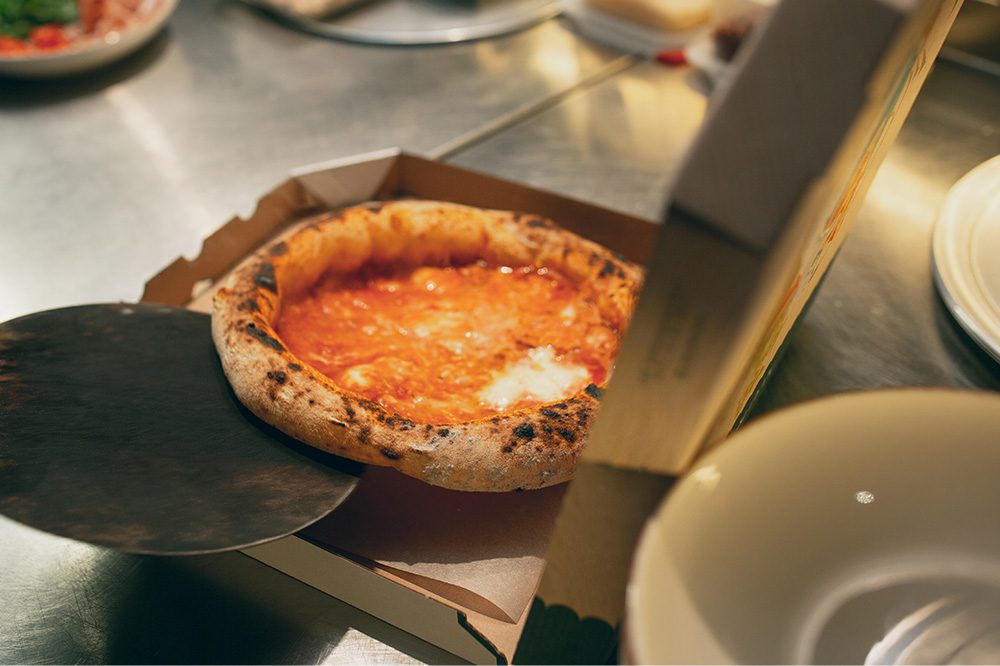 Freshly baked pizza being boxed in a commercial kitchen, representing food kept warm and ready to serve with Hoshizaki reach-in heated cabinets.