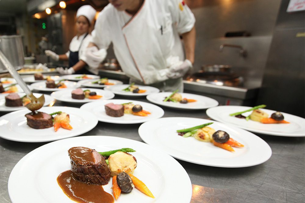 Chefs plating gourmet meals in a high-volume kitchen supported by Hoshizaki pass thru refrigeration.