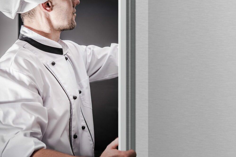 Chef opening a stainless steel Hoshizaki refrigerator, showcasing commercial kitchen use and durable Steelheart® construction.