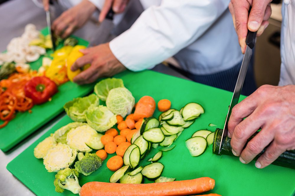 Chefs prepping fresh vegetables in a commercial kitchen supported by Hoshizaki undercounter refrigerators for easy cold storage access.