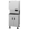 A stainless steel commercial ice and water dispenser with control buttons, a dispensing area, and a storage cabinet below.