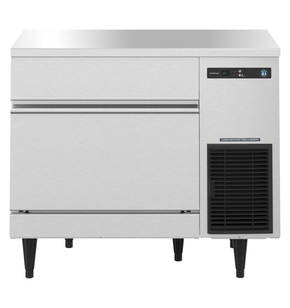 Stainless steel commercial ice machine with a front panel, control display, ventilation grille, and four black legs.
