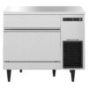 Stainless steel commercial ice machine with a front panel, control display, ventilation grille, and four black legs.